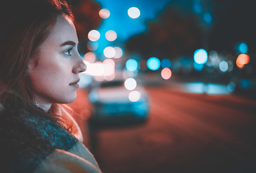 side view of thoughtful woman looking at city lights at night in dark