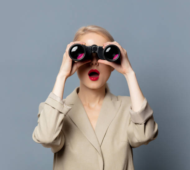 istock Style blonde in jacket with binoculars on gray background 1279709997