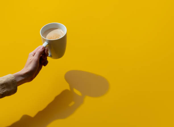 female hand holds cup of coffee on yellow background - coffee top view imagens e fotografias de stock