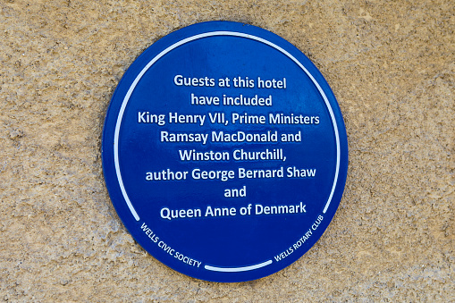 Wells, UK - March 16th 2020: A blue plaque on the exterior of the Swan Hotel in the city of Wells, detailing its former famous guests.
