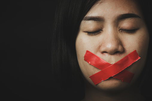 Asian woman blindfold wrapping mouth with red adhesive tape on black background. Freedom speech censorship and stop talk, International Human Right day