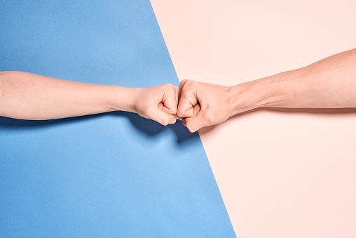 Two fists against each other. Arm photographed on two-part background. The background is in two colours that highlight the diversity. Pictured on a split background. Divided into two different colours that divide the image in the middle. The background is very symmetrical and graphic