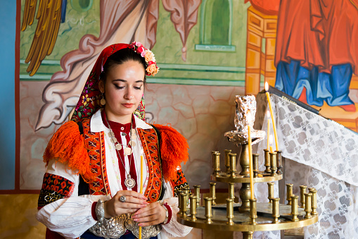 A young, beautiful woman dressed in a Bulgarian national costume, photographed in an Orthodox church.
