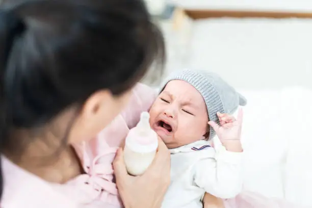 Photo of Close up view of beautiful Asian mother and her crying lovely newborn baby. Mother holding her baby and feeding cute newborn baby from milk bottle. Happy family concept.