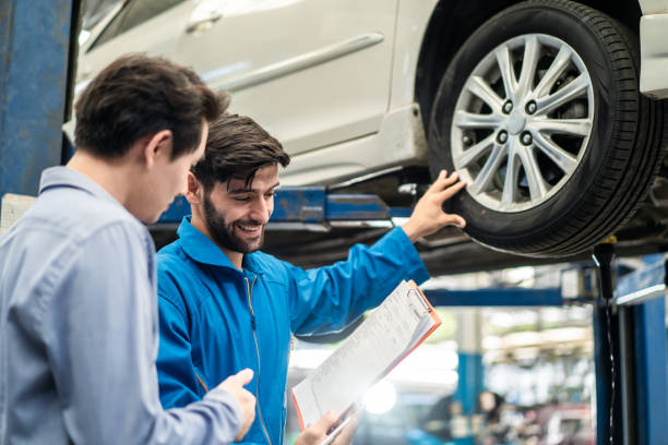 entretien du véhicule beau serviceur homme expliquer l’état de la voiture et les dépenses de sourire client masculin dans le garage avant de signer le document de quatation de réparation automobile. concept d’entreprise de service de réparation de - auto repair shop customer auto mechanic mechanic photos et images de collection