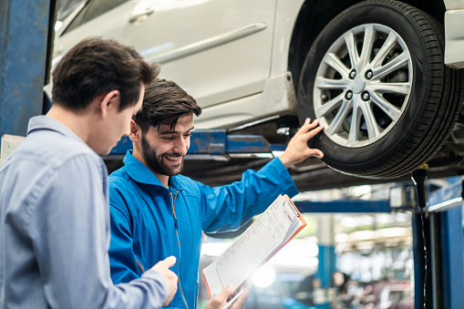 Vehicle maintenance handsome man servicer explain car condition and expense to smile male customer in garage before sign automotive repair quatation document. Vehicle repair service business concept.