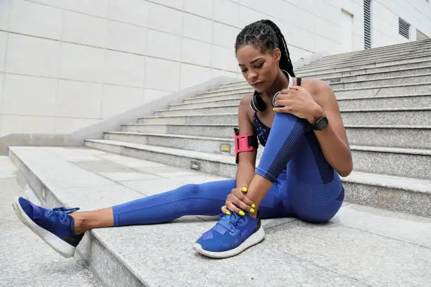 Fit young Black sportswoman suffering from pain in her ankle after morning jog