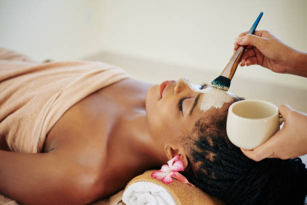 Beautician applying clay mask Close-up image of beautician applying deep clearing clay mask on face of Black young woman facial mask stock pictures, royalty-free photos & images