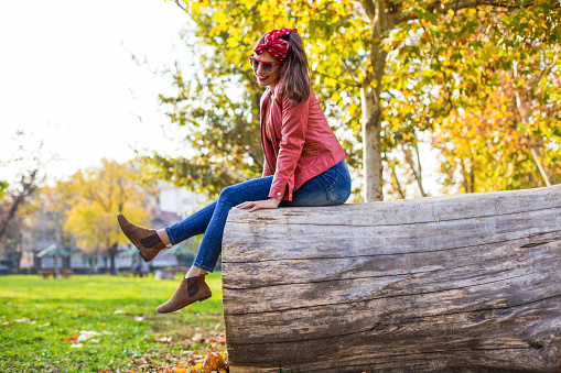 Beautiful young casually dressed woman sitting and relaxing in the city park on a lovely autumn day