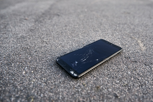 Damaged smartphone with broken touch screen on the asphalt