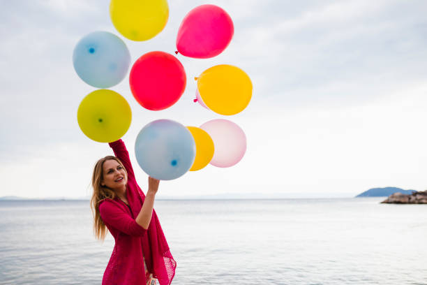 istock Woman with multi-colored balloons having fun at the beach 1279747364
