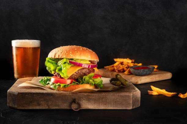 Burger and beer. Hamburger with beef, cheese, onion, tomato, and green salad, with pickles and French fries, a side view on a black background Burger and beer. Hamburger with beef, cheese, onion, tomato, and green salad, with pickles and French fries, a side view on a black background with a place for text spanish hamburger stock pictures, royalty-free photos & images