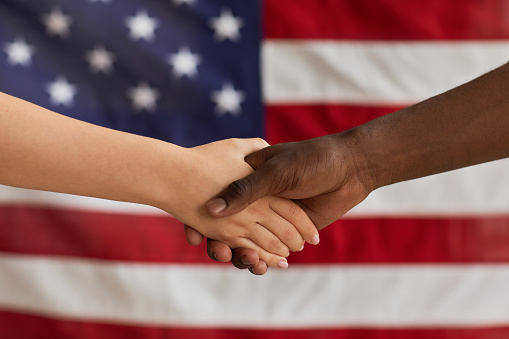 Close-up of people shaking hands against the American flag