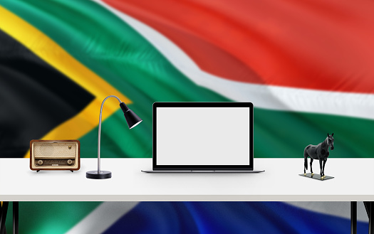 South Africa national flag background with workspace, desktop computer and office accessories on white modern table.