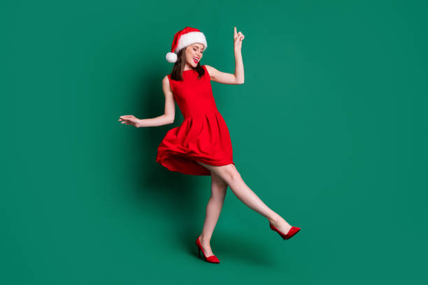 かわいい魅力的な女性の新年パーティーのお祝いの良い気分ダンスディスコの人気曲のフルボディ写真は、サンタキャップ赤のミニドレスの衣装スティレット孤立した緑の色の背景