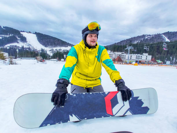 istock man with snowboard sitting at snowed hill 1279761069