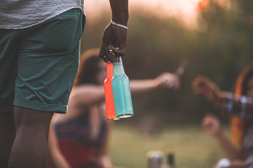 Close up of colorful bottles of refreshing drinks that a man in shorts is carrying to surprise their friends during a picnic.