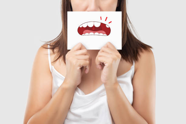 Asian woman in the red shirt holding a brown paper with the broken tooth cartoon picture of his mouth against the gray background, Decayed tooth, The concept with healthcare gums and teeth Asian woman in the red shirt holding a brown paper with the broken tooth cartoon picture of his mouth against the gray background, Decayed tooth, The concept with healthcare gums and teeth bad teeth stock pictures, royalty-free photos & images