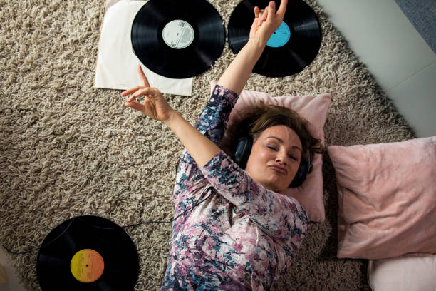 Woman enjoying her old vinyl records Directly above of mid adult woman lying on the floor of her living room and enjoying the music played from a modern LP player during isolation at home woman lying on the floor isolated stock pictures, royalty-free photos & images