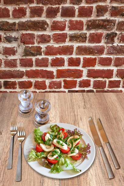 Rustic wooden table with a set of silverware , White plate with tomatoes and mozzarella on salad.