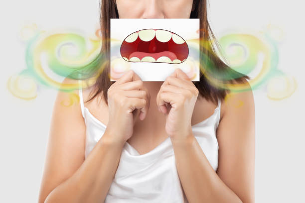 Bad breath or Halitosis A woman wearing white dress holding a white paper with an open mouth cartoon image. On a light gray background. Bad breath or Halitosis. The concept with healthcare gums and teeth speak no evil stock pictures, royalty-free photos & images
