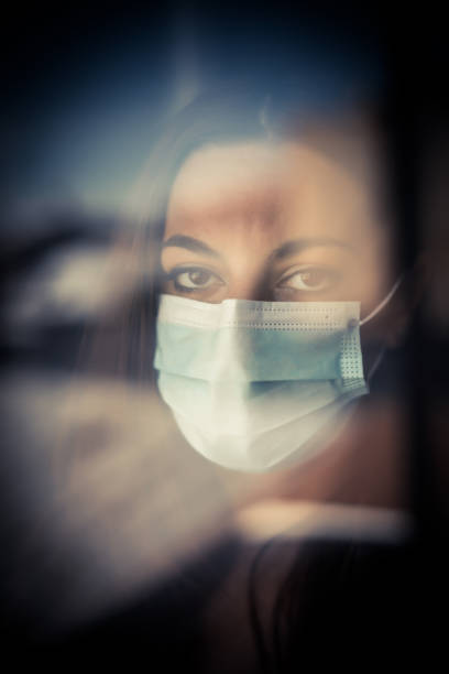 istock Woman wearing a surgical mask by a window 1279766941