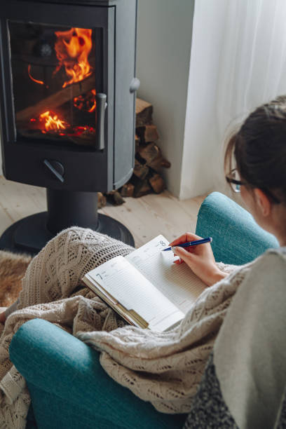 istock Young woman  write in notebook sitting in armchair by fireplace 1279768149