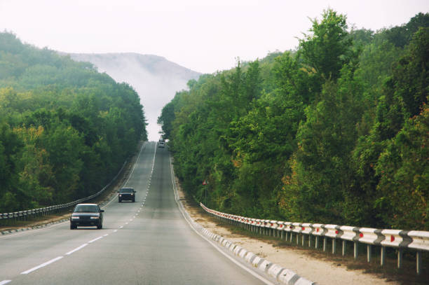 Asphalt road with moving cars against misty mountains.