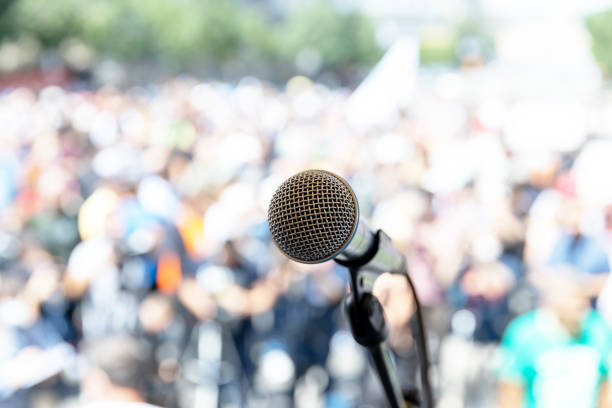 istock Focus on microphone, blurred group of people at mass protest 1279772801