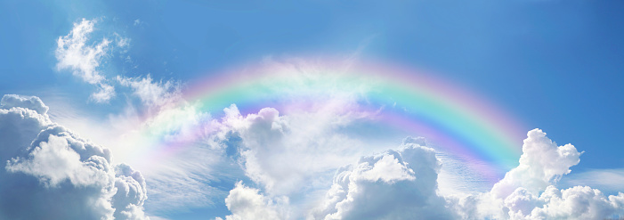 big fluffy clouds with a giant arcing rainbow against a  beautiful summer time blue sky with copy space for messages