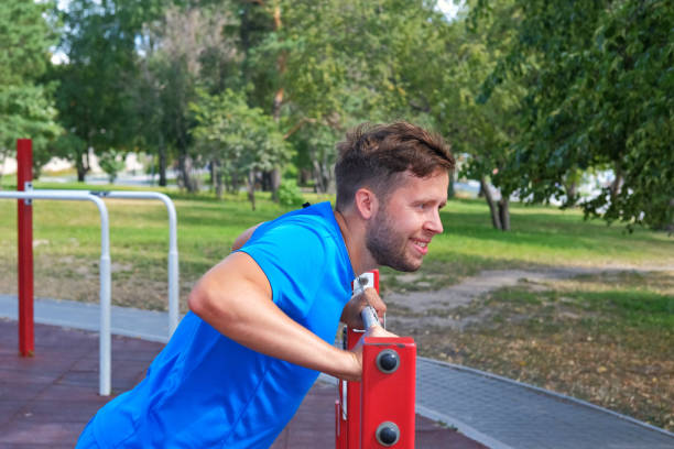 athletic man in blue sportswear doing push-ups from the horizontal bar in the park on the playground. - exercising men push ups muscular build imagens e fotografias de stock