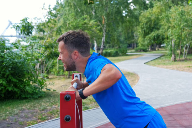 athletic man in blue sportswear doing push-ups from the horizontal bar in the park on the playground. - exercising men push ups muscular build imagens e fotografias de stock