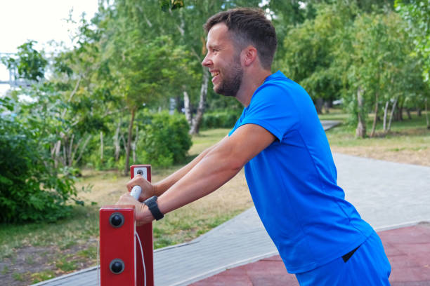 athletic man in blue sportswear doing push-ups from the horizontal bar in the park on the playground. - exercising men push ups muscular build imagens e fotografias de stock