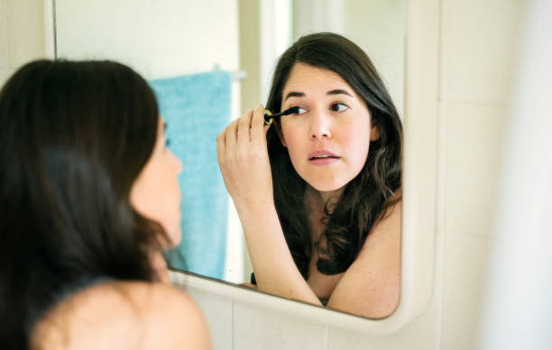 istock Young woman putting on mascara in a bathroom mirror 1279783078