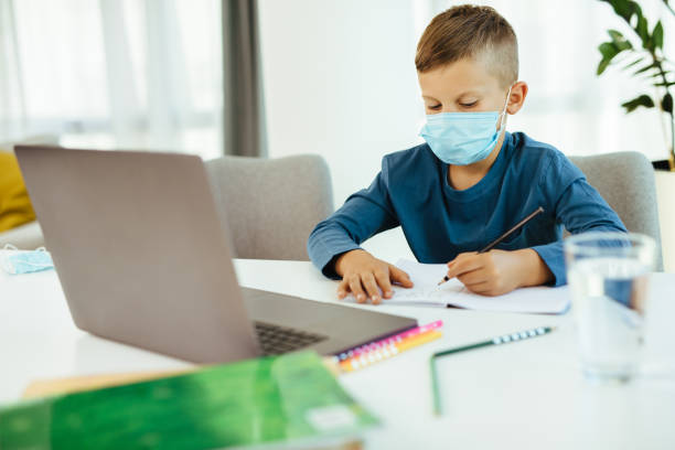 istock School boy with face mask watching online education classes on laptop 1279786771