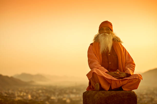 Unidentified Shadu Baba poses for camera while prayer during sunrise with soft image back ground of Pushkar town at Savitri Temple in Pushkar, India.