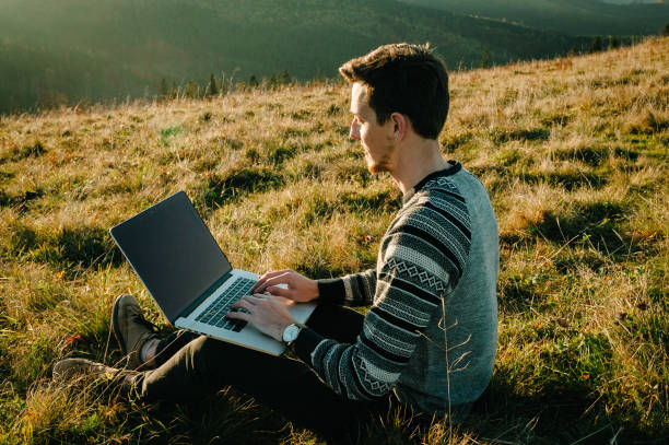 istock Man working outdoors with laptop sitting in mountains. Concept of remote work or freelancer lifestyle. Cellular network broadband coverage. internet 5G. Hiker tourist enjoying valley view sunset. 1279789262