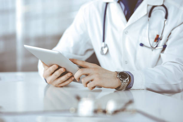 istock Unknown male doctor sitting and working with tablet computer in clinic at his working place, close-up. Young physician at work. Perfect medical service, medicine concept 1279790752