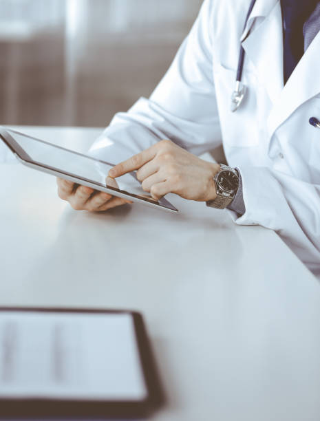 istock Unknown male doctor sitting and working with tablet computer in clinic at his working place, close-up. Young physician at work. Perfect medical service, medicine concept 1279790762