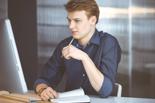 istock Young blond businessman thinking about strategy at his working place with computer. Startup business means working hard and out of time for success achievement 1279790783