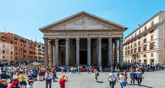 Rome, Italy - June 1, 2014: Woman is playing harp with tourists gather around fountain in bright Italian plaza in front of the Pantheon, Rome, Italy.  Tourists gather around the Fontana del Pantheon under bright blue skies. The plaza, Piazza della Rotunda is named after the informal title of the Pantheon, Church of Santa Maria Rotonda, one of the top tourist attractions in the city.