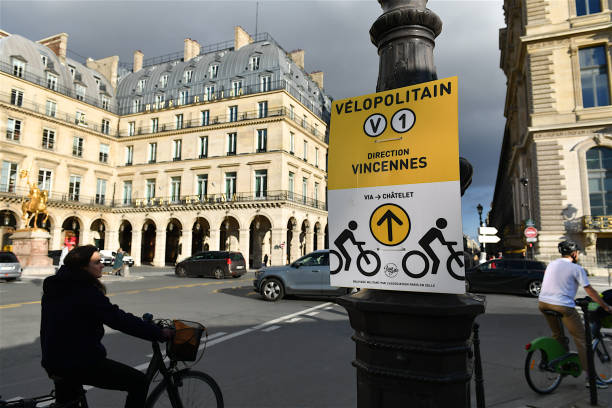 Bicycle lane direction sign in Paris, France. Paris, France-10 11 2020:People riding bicycles with direction sign on one of the many cycle paths on rue de Rivoli in the French capital. place des pyramides stock pictures, royalty-free photos & images
