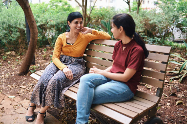 istock Happy looking sisters discussing while sitting on a bench in public park 1279793580