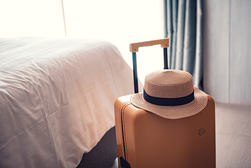 Suitcase or luggage bag with hat in a modern hotel room - relaxing time, holidays, weekend and traveling concept.