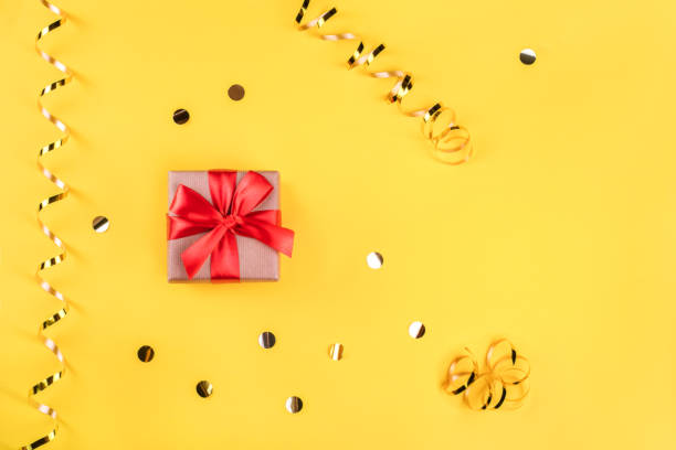 istock Red gift box on yellow background with golden confetti. 1279796023
