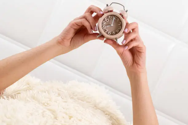 Photo of Alarm clock in female hands in a white bed, the concept of time, a wonderful start to a new day, good morning