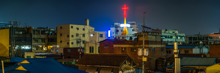 Neon red cross glowing over the rooftops and the crowded highrise cityscape of central Seoul at night, South Korea.