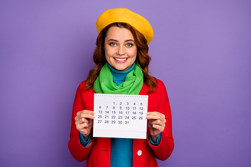 Close-up portrait of her she nice attractive lovely pretty charming cheerful cheery, wavy-haired girl holding in hands paper calendar isolated on violet lilac purple pastel color background