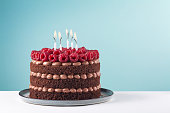 Chocolate birthday cake with raspberries and candles on  white table and blue background. Copy space.