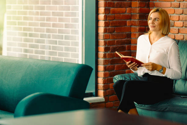 istock Young confident woman entrepreneur enjoys the work break while sitting on leather sofa in office interior, intelligent awesome female lawyer in formal wear reading a book during work break 1279807841